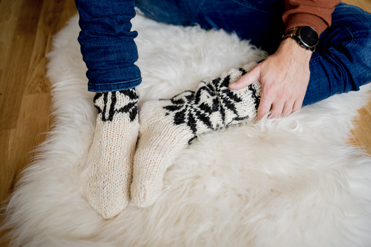 Man in woollen turtleneck and woollen cream star patterned knitted socks sitting on natural sheepskin rug. Men is feeling warm and cosy on winter time