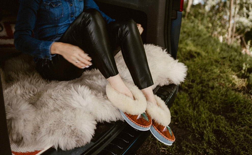 Girl sitting in a Van on the sheepskin rug. She is wearing sheepskin moccasins, Van Life Inspiration and nature escape wool  product ideas 