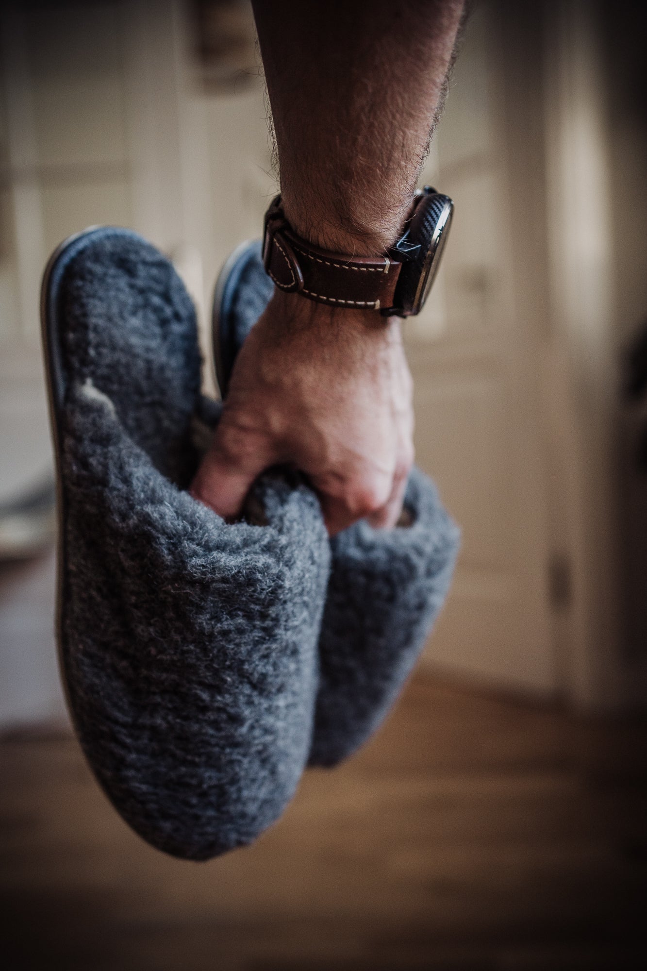 Men's grey wool slippers held in a man's hand