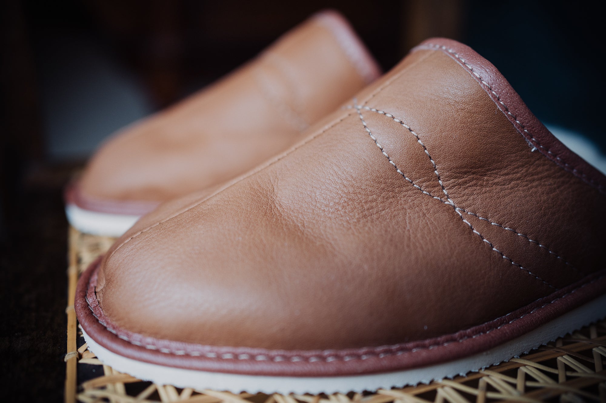 Close-up of fine stitching on soft leather men's slippers.