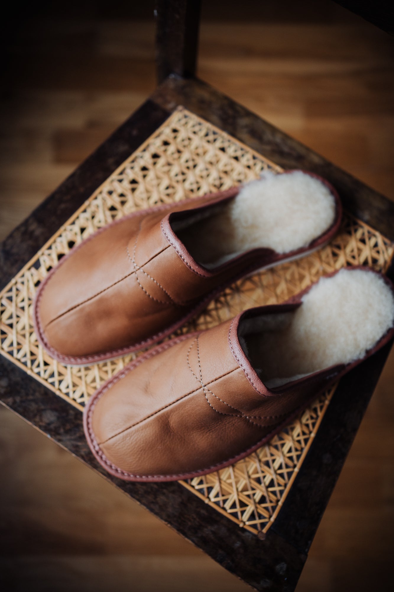 Soft men's leather slippers with cream wool lining, elegantly displayed on a nice chair.