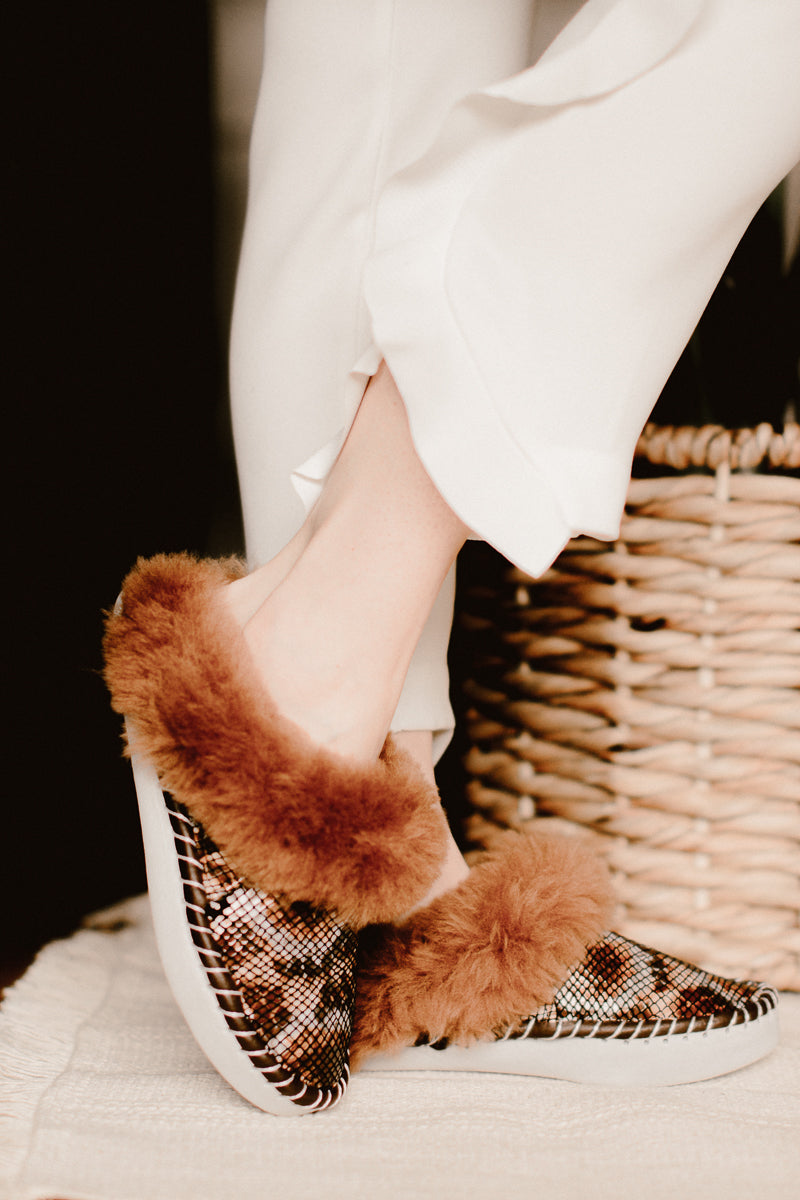 Women's feet adorned with brown snake pattern Bamboshe sheepskin slippers.
