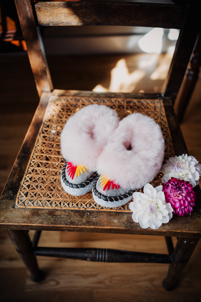 Fluffy girls' sheepskin slippers with pink fur, placed on a chair adorned with dahlia flowers decoration.
