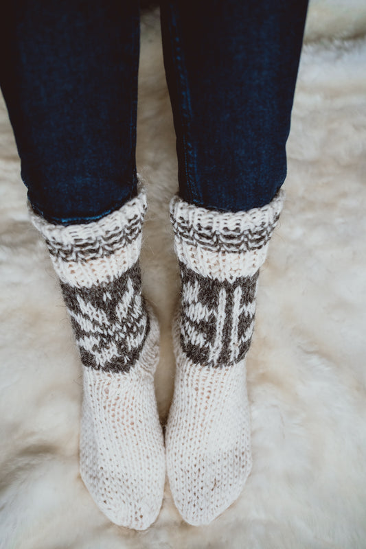 Women's feet wearing cream hand-knitted wool socks, resting on a sheepskin rug.
