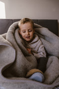Load image into Gallery viewer, Little boy is very happy and feeling cosy. Wrapped in pure merino very thick wool blanket, wearing sheepskin slippers and woollen jumper
