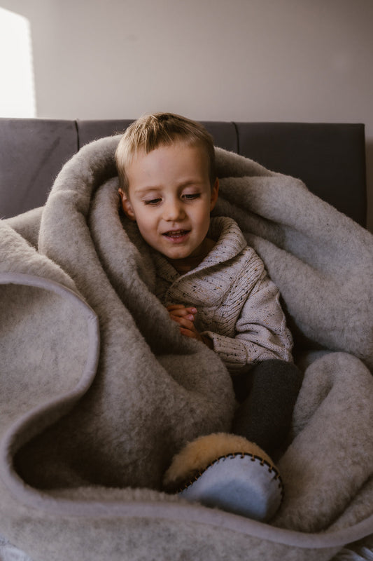 Little boy is very happy and feeling cosy. Wrapped in pure merino very thick wool blanket, wearing sheepskin slippers and woollen jumper