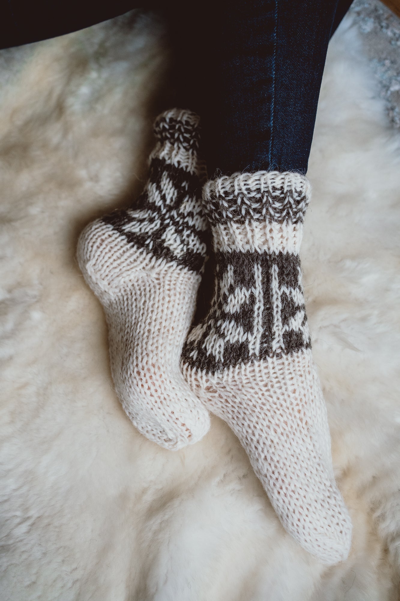 Women's feet wearing cream hand-knitted wool socks, resting on a sheepskin rug.